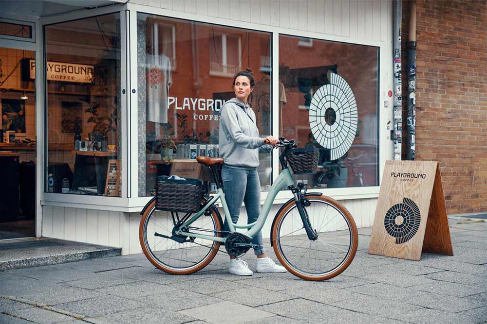 Eine Frau steht mit einem Riese und Müller e-Bike vor einem Café