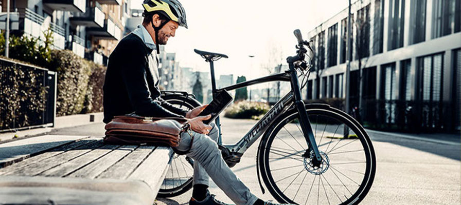 Ein Mann sitzt auf einer Bank und schaut auf sein Tablet. Neben ihm steht ein Specialized e-Bike